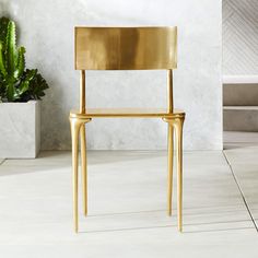 a gold chair sitting on top of a white floor next to a potted plant