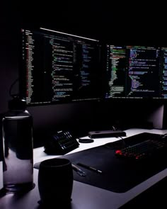 two computer monitors sitting next to each other on top of a desk in the dark