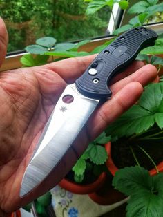 a person holding a knife in their hand next to some plants and potted plants