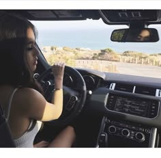 a woman sitting in the driver's seat of a car with her hand on the steering wheel