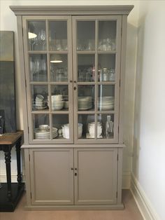 a gray china cabinet with glass doors and dishes on the top shelf in front of it