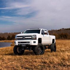 a white truck parked on top of a dry grass field next to a body of water