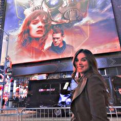 a woman standing in front of a giant movie poster on the side of a building