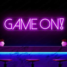 a neon sign that says game on above three stools