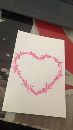 a piece of paper with a pink heart drawn on it next to a laptop computer