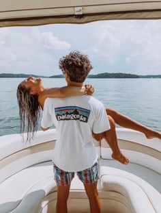 a man and woman embracing while standing on the back of a boat in the water