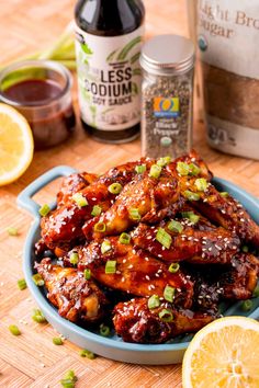 the chicken wings are covered in sauce and garnished with scallions, green onions, and sliced lemons