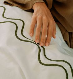 a person's hand on top of a bed with white sheets and green lines