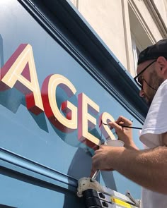 a man is painting the side of a large blue sign that says agers on it