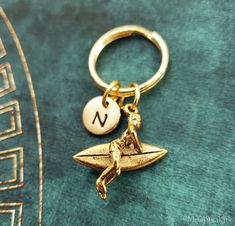 a gold keychain with a letter on it and a small airplane charm attached to it