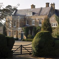 a large house with hedges in front of it and a gate leading into the yard