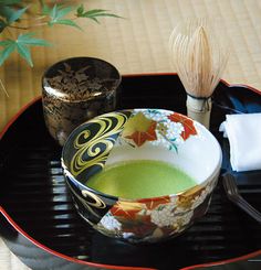 a bowl with green liquid in it sitting on top of a black tray next to a brush