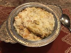 a silver bowl filled with mashed potatoes on top of a red place mat next to a spoon