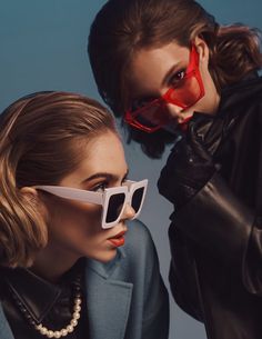 two women in black jackets and white sunglasses, one with red glasses on her face