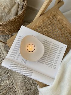 an open book with a lit candle sitting on top of it next to a wicker basket