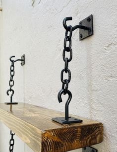 a wooden shelf with chains hanging from it's sides and two hooks on the wall