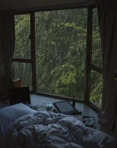 a laptop computer sitting on top of a bed in front of a window next to a forest