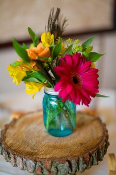 colorful flowers are in a mason jar on a tree stump