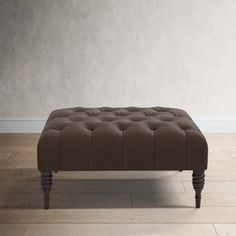 a brown ottoman sitting on top of a hard wood floor next to a white wall