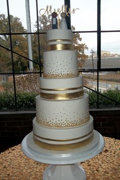 a white and gold wedding cake sitting on top of a table next to a window