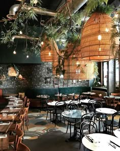 the interior of a restaurant with tables, chairs and plants hanging from the ceiling above