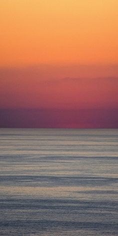 the sun is setting over the ocean with an airplane flying in the sky above it