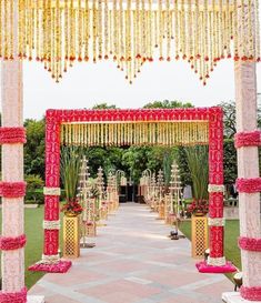 an outdoor wedding venue decorated with red and white flowers, gold decorations and hanging chandeliers