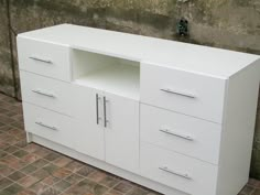 a white cabinet sitting on top of a brick floor next to a wall with a sink and faucet