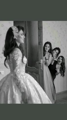 a woman in a wedding dress is looking at herself in the mirror while two other women look on