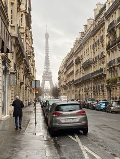 a man walking down the street next to parked cars in front of the eiffel tower