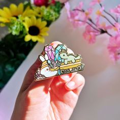 a person holding up a pin with an elephant on it and flowers in the background