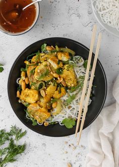 a black bowl filled with noodles and vegetables next to chopsticks on a white surface