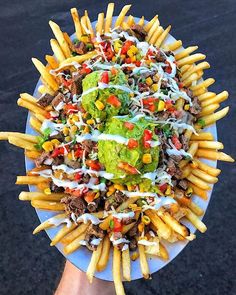 a person holding a plate with french fries and taco salad on it