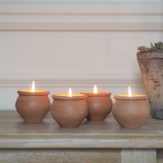 four clay pots with lit candles in them on a table