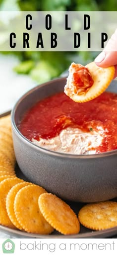 a hand dipping some crackers into a bowl of dip with cheese and tomato sauce