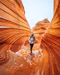 a woman standing in the middle of a canyon with red rock formations behind her and snow on the ground