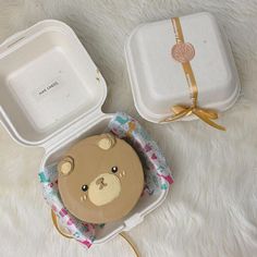 a brown teddy bear in a white box with a gold ribbon around it's neck