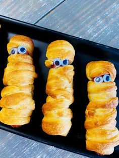 three croissants with googly eyes are on a black tray