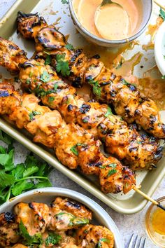 grilled chicken skewers on a tray with dipping sauce and cilantro