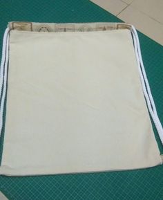 a drawstring bag sitting on top of a green mat with white trimming