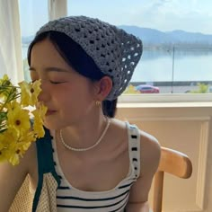 a woman sitting at a table with flowers in front of her face and wearing a hat