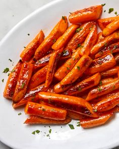 a white plate topped with sliced carrots covered in bbq sauce and garnished with parsley