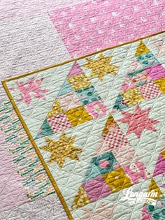 a pink and yellow quilt on top of a white table cloth with stars in the center