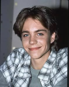 a young man with blue eyes smiles at the camera while wearing a flannel shirt