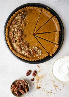 a pie sitting on top of a table next to a bowl of whipped cream and pecans