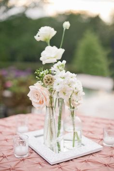 white flowers in vases sitting on top of a pink table cloth covered tablecloth