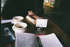 an open book sitting on top of a wooden table next to cups and saucers