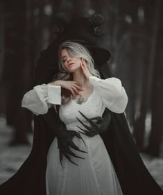 a woman in a white dress and black coat with horns on her head is posing for the camera