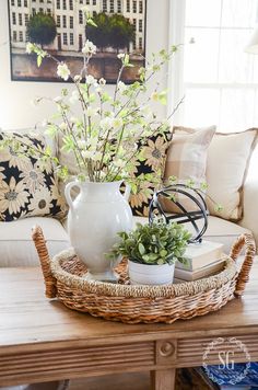 a white vase sitting on top of a table next to a basket filled with flowers