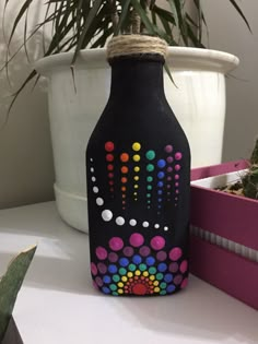 a painted bottle sitting on top of a table next to a potted plant